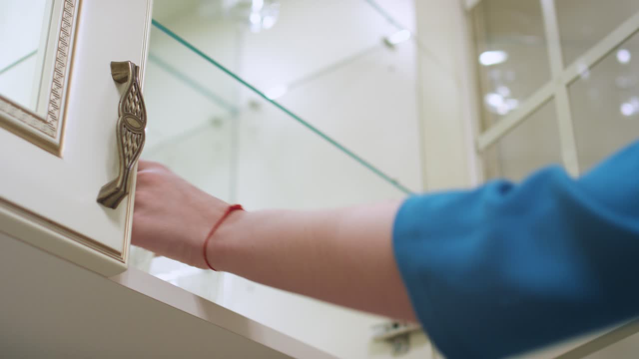 mujer mano abriendo la puerta del armario de la cocina y tomando vidrio por el estante dentro