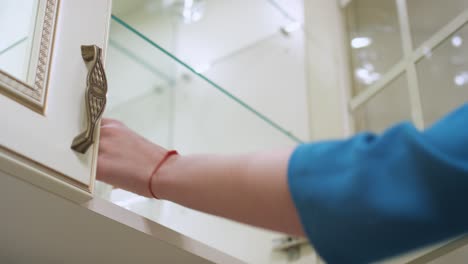 woman hand opening kitchen cupboard door and taking glass by shelf inside