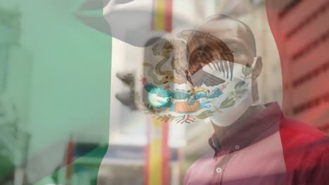 Animation-of-flag-of-mexico-waving-over-african-american-man-wearing-face-mask-in-city-street