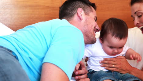 padres felices besando a su bebé en la cama