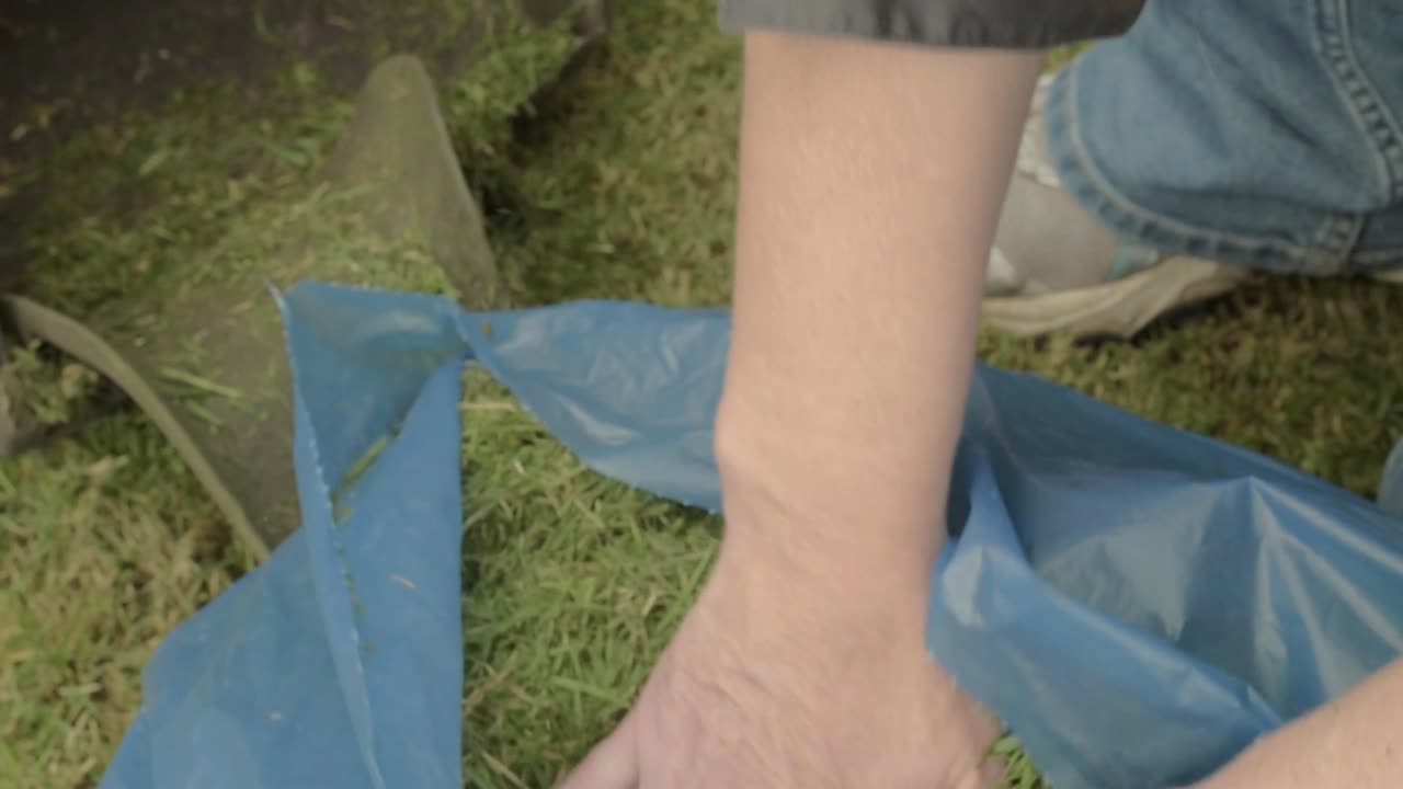 갓 자른 잔디의 잔디 깎는 기계를 청소하는 정원사