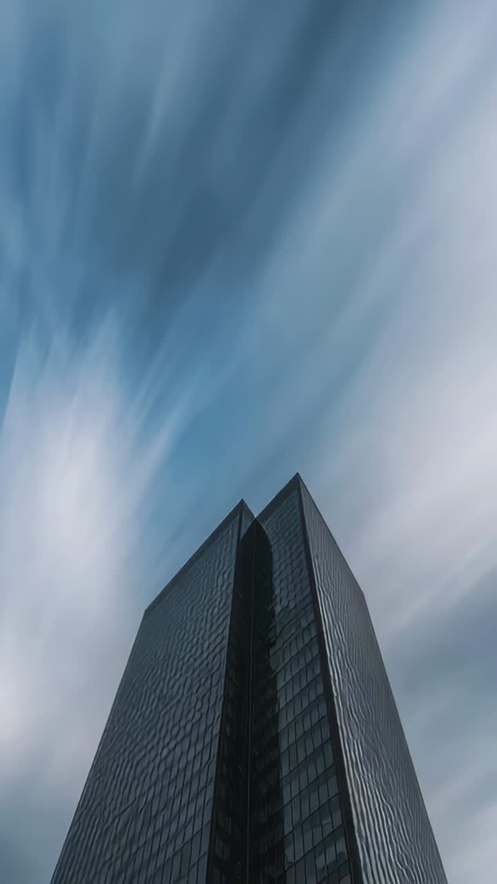 Vertical video: Tilting camera showing glass-clad skyscraper at street, revealing brief blue patch