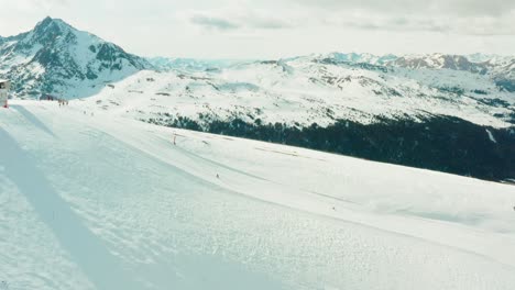 Flyling-over-a-ski-slope-with-people-skiing-down,-revealing-the-valley-behind