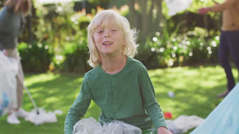 video portrait of smiling caucasian boy collecting plastic for recycling with family outdoors