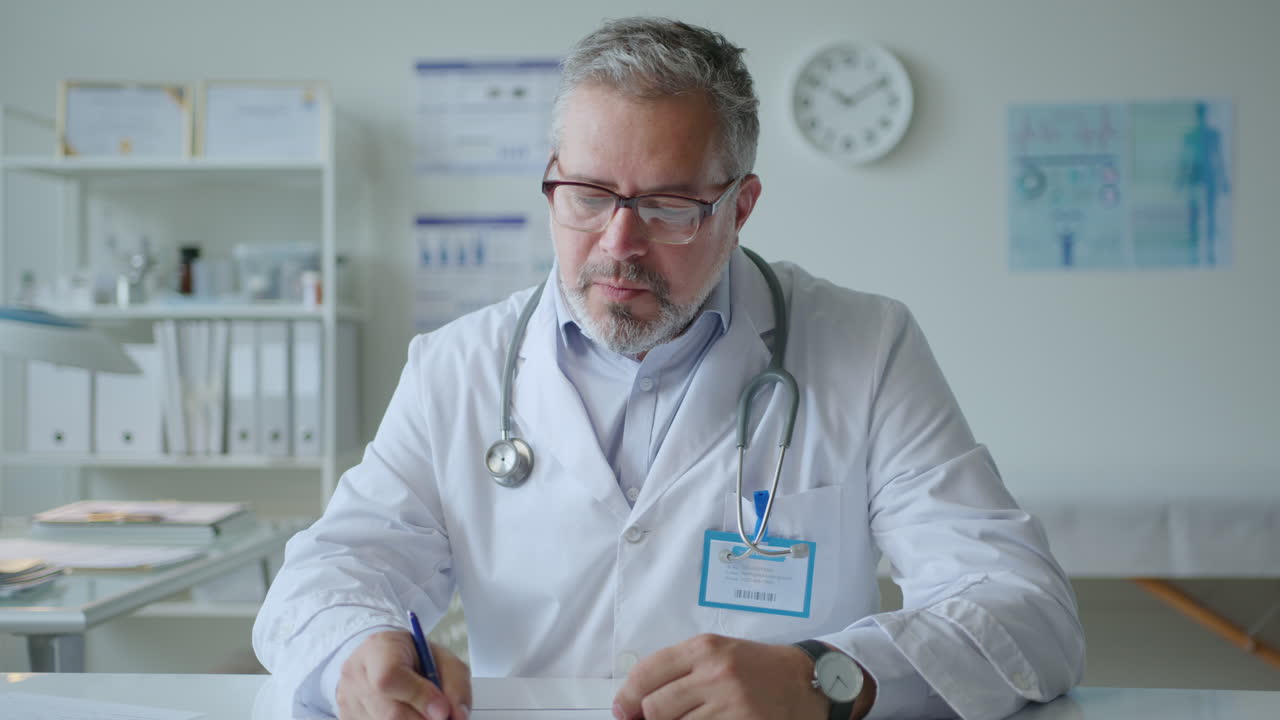 Mid-Aged Doctor Sitting in Clinic and Giving Online Consultation