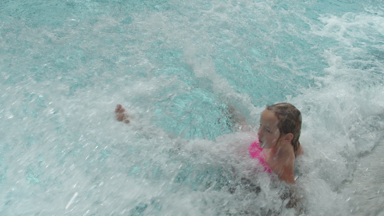 Premium stock video - A little girl slides down a steep kamikaze slide and falls uncontrollably through the water