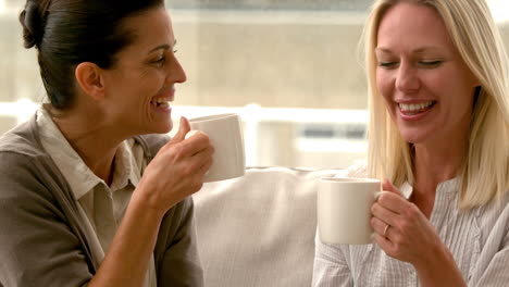 In-slow-motion-two-friends-sitting-on-the-couch-chatting-over-coffee-at-home