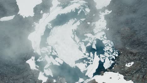 top-down view of a mountain lake with ice floes and fog