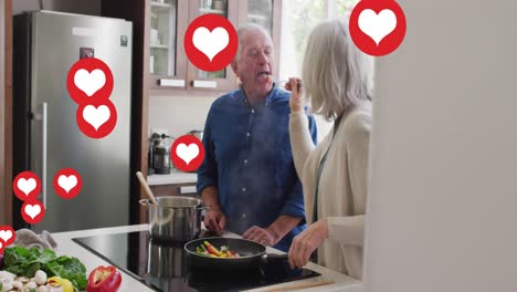 Animation-of-social-media-heart-icons-over-senior-couple-cooking-in-kitchen