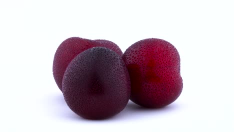 Three big purple maynard plums with water drops rotating on the turntable. Isolated on the white background. Closeup.