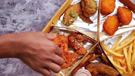 mano metiendo la mano en una caja de entrega de alimentos llena de alas de pollo, papas fritas y nuggets