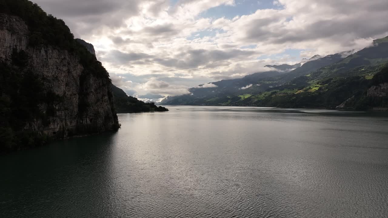 Aerial view showcases the serene turquoise waters of Walensee, Switzerland, nestled between steep, majestic mountains. The panoramic scene highlights the fjord-like landscape, with lush green slopes
