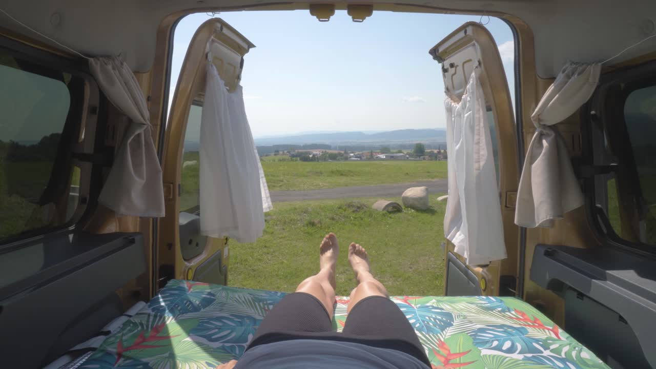 녹색 풍경이 내려다보이는 캠퍼 밴의 매트리스에 누워 있는 여성의 정적인 클로즈업