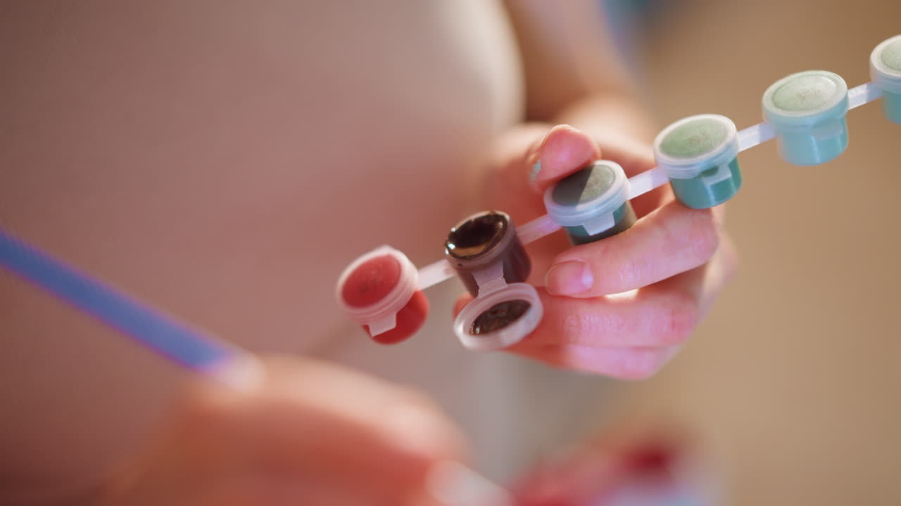 Close Up Hands Selecting Nail Polish Palette, Manicurist Painting Color Swatches On Tip Wheel, Soft Salon Lighting, Glossy Pigments And Precise Brush Strokes, Intimate Pampering Atmosphere