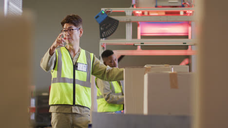 diverse male workers wearing safety suits with boxes on conveyor belt in warehouse