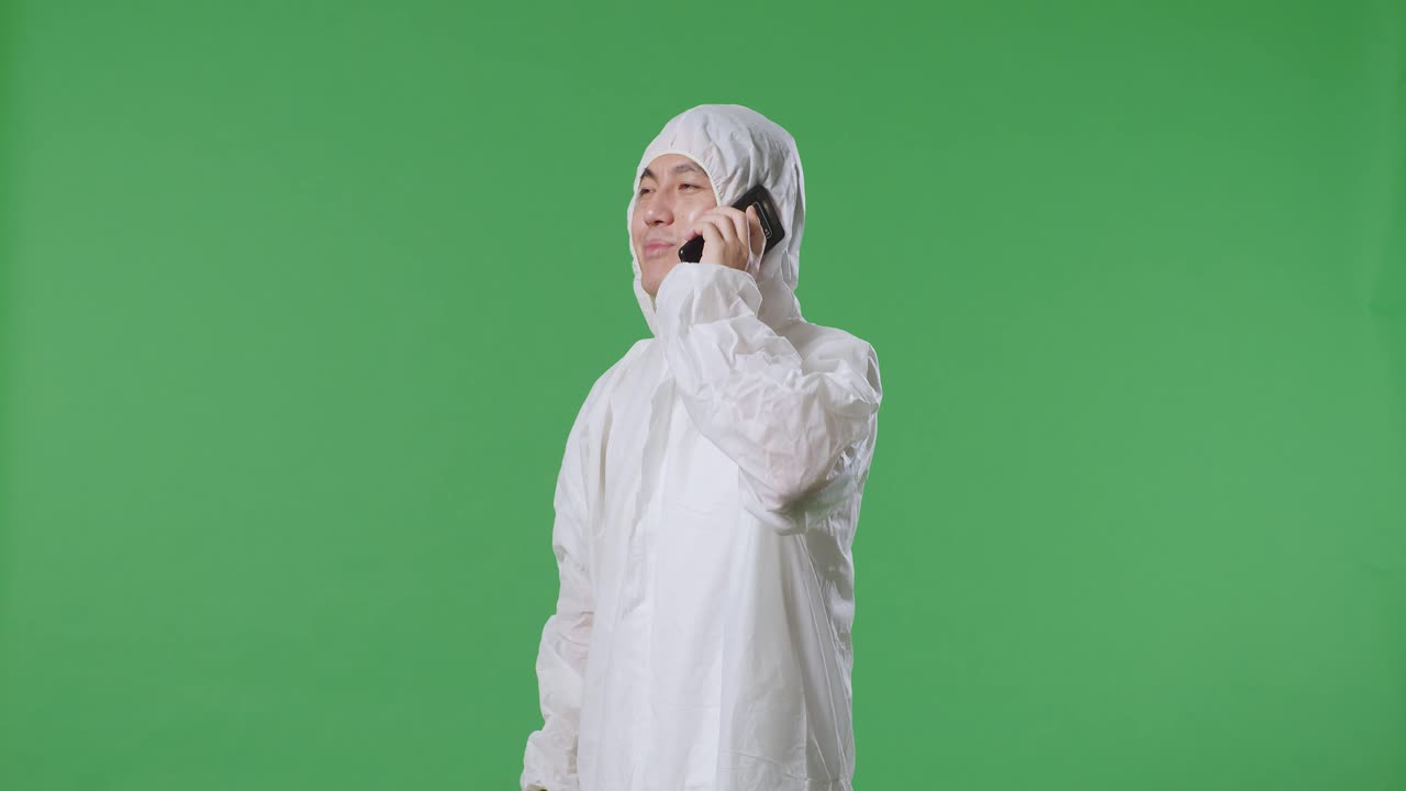 녹색 화면 배경에 서서 스마트폰으로 대화하는 아시아 남성 과학자의 측면 시각