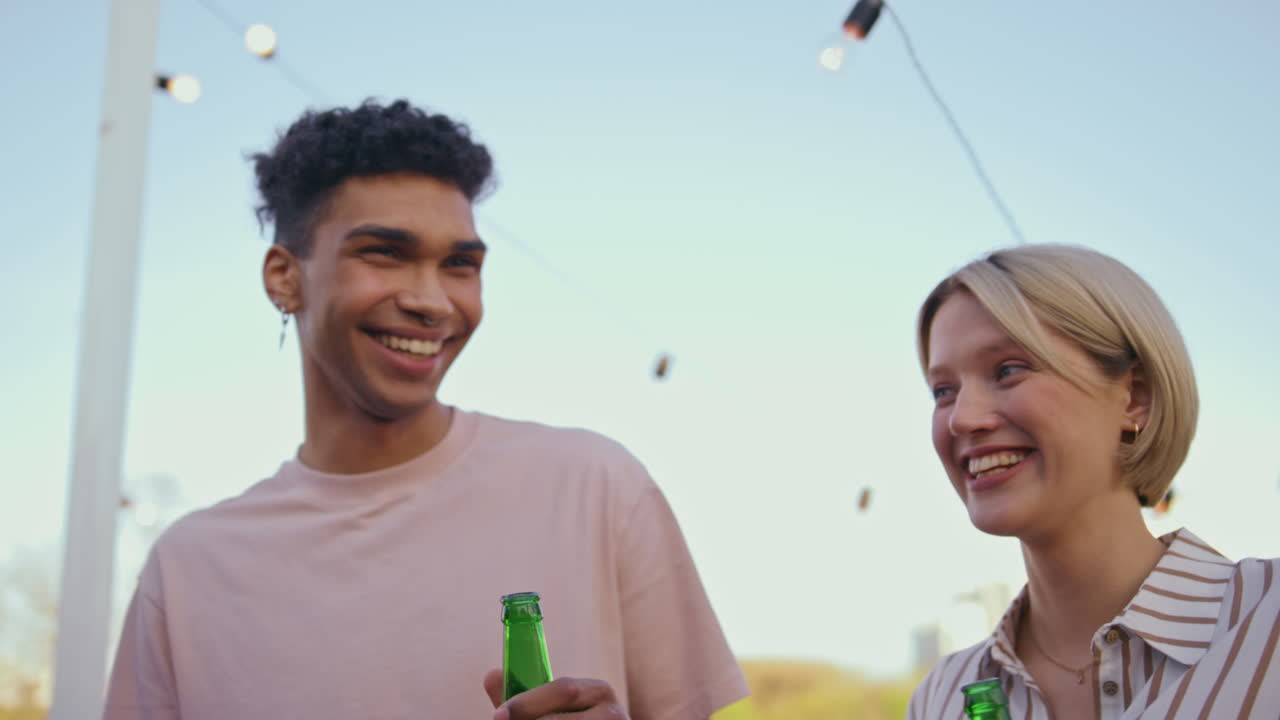 una pareja diversa bebiendo cerveza en una terraza de primavera. una mujer emocional riendo.