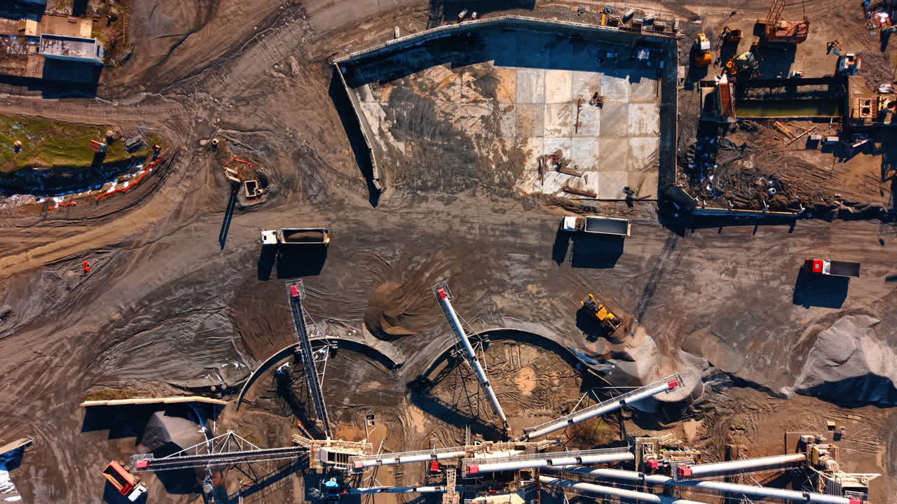 Heavy truck and loader working at industrial granite quarry. Aerial shot of dump trucks and a yellow front loader moving stone near a crushing plant