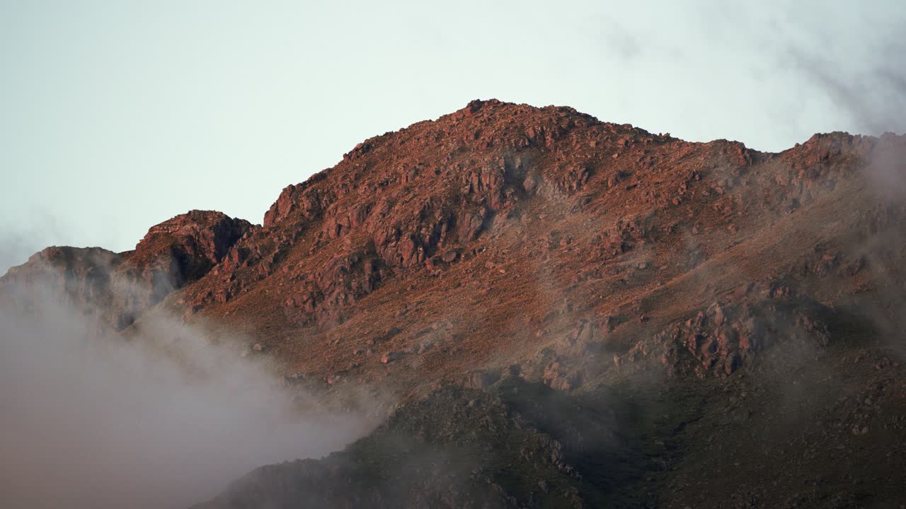 A serene timelapse capturing low clouds drifting across the rugged peaks of the Sierra de los Comechingones during sunset near Merlo, San Luis