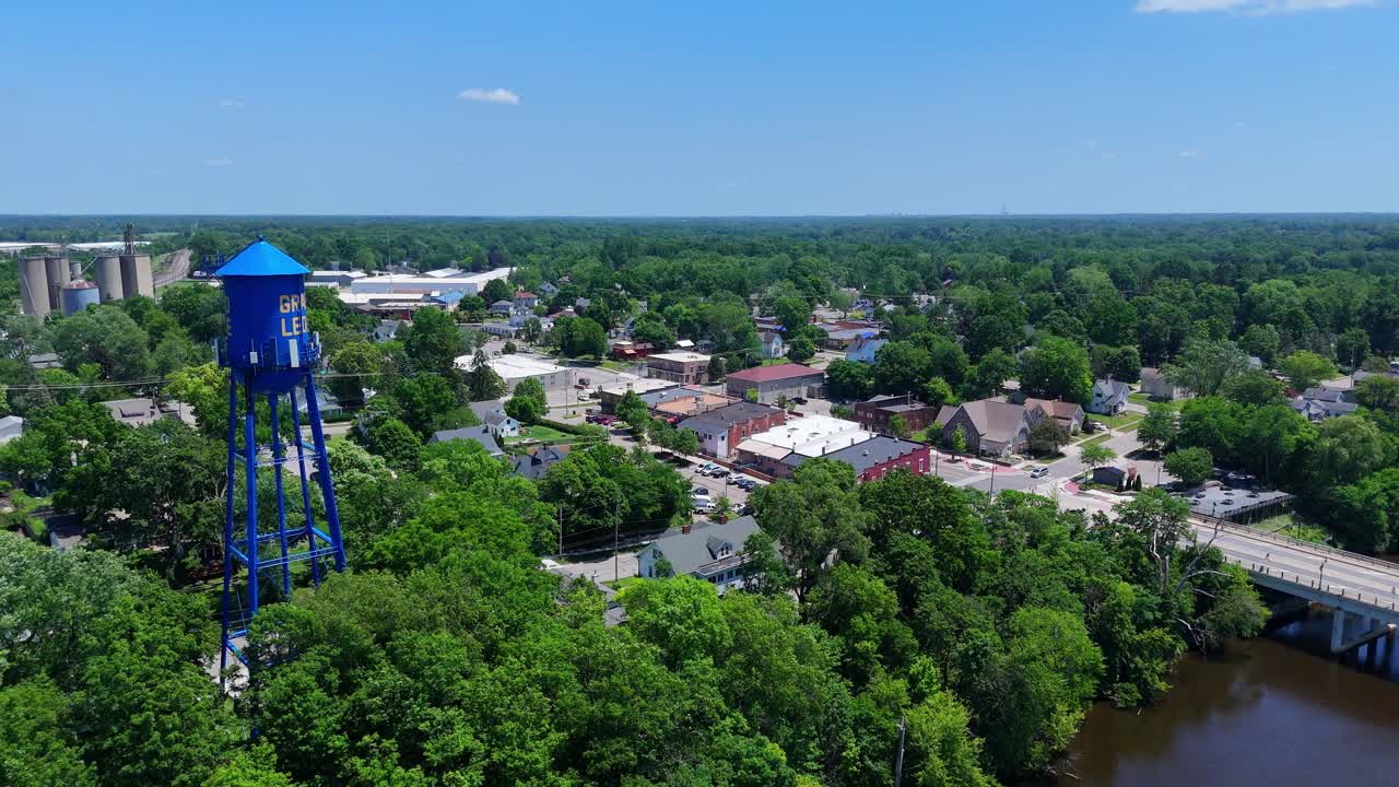 A blue water tower with "GRAND LEDGE" written on above green treetops in Michigan from above