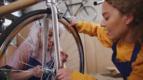 female apprentices in workshop checking wheel of hand built bicycle frame