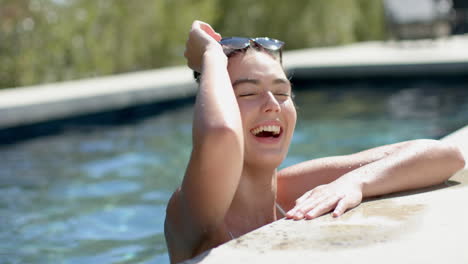 a teenage caucasian girl is laughing by a poolside, her wet hair slicked back