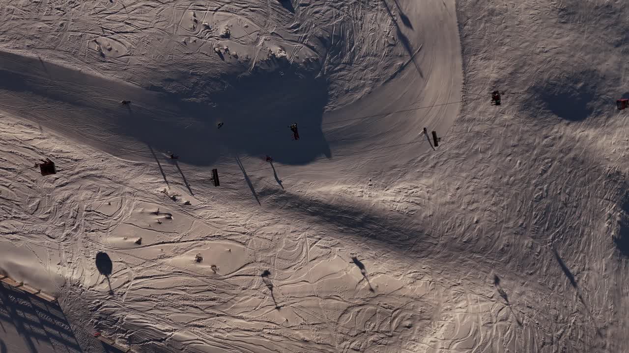 People skiing and snowboarding at Cardrona ski resort at sunrise, tracks in snow and long shadows. New Zealand. aerial top-down view