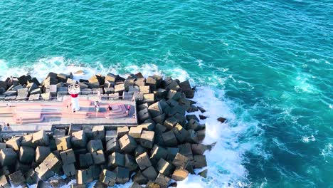 drone footage of waves crashing against a rock jetty in clear blue waters.