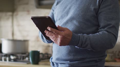 Midsection-of-caucasian-man-using-tablet-in-kitchen-at-home