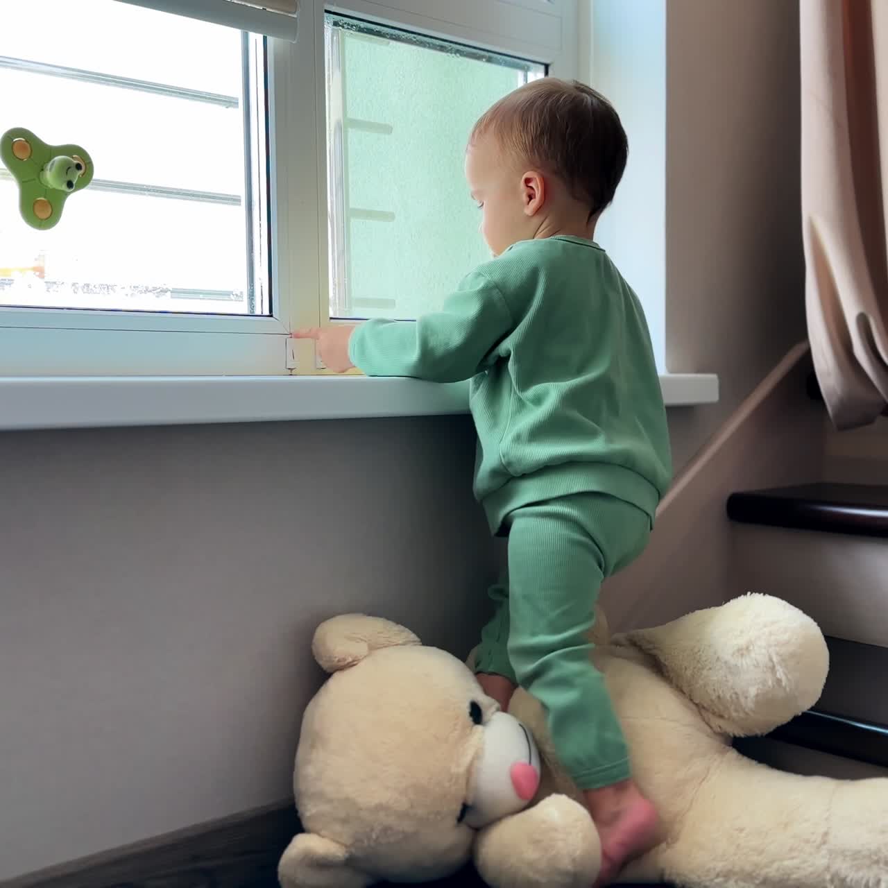 One year old toddler plays near the window indoors. Barefoot child stands on a big white soft teddy bear
