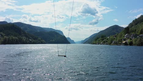 tall swing moving slowly from side to side with amazing scenic veafjorden in background - static aerial with swing close to fjord surface - norway