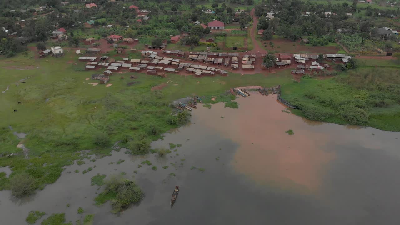 Plano aéreo avançando sobre as margens do Lago Vitória até uma pequena vila de pescadores em terra