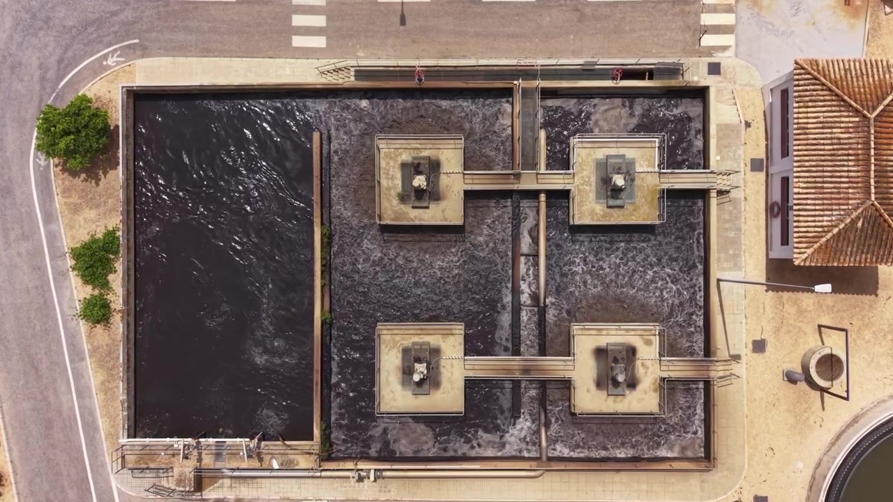 Overhead view of urban wastewater treatment plant aeration basin with activated sludge, mechanical aerators creating turbulence in divided tank sections