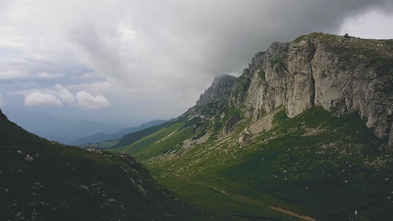 disparo hacia atrás de drones que revela una cresta de montaña con nubes bajas y un valle alpino con hierba verde