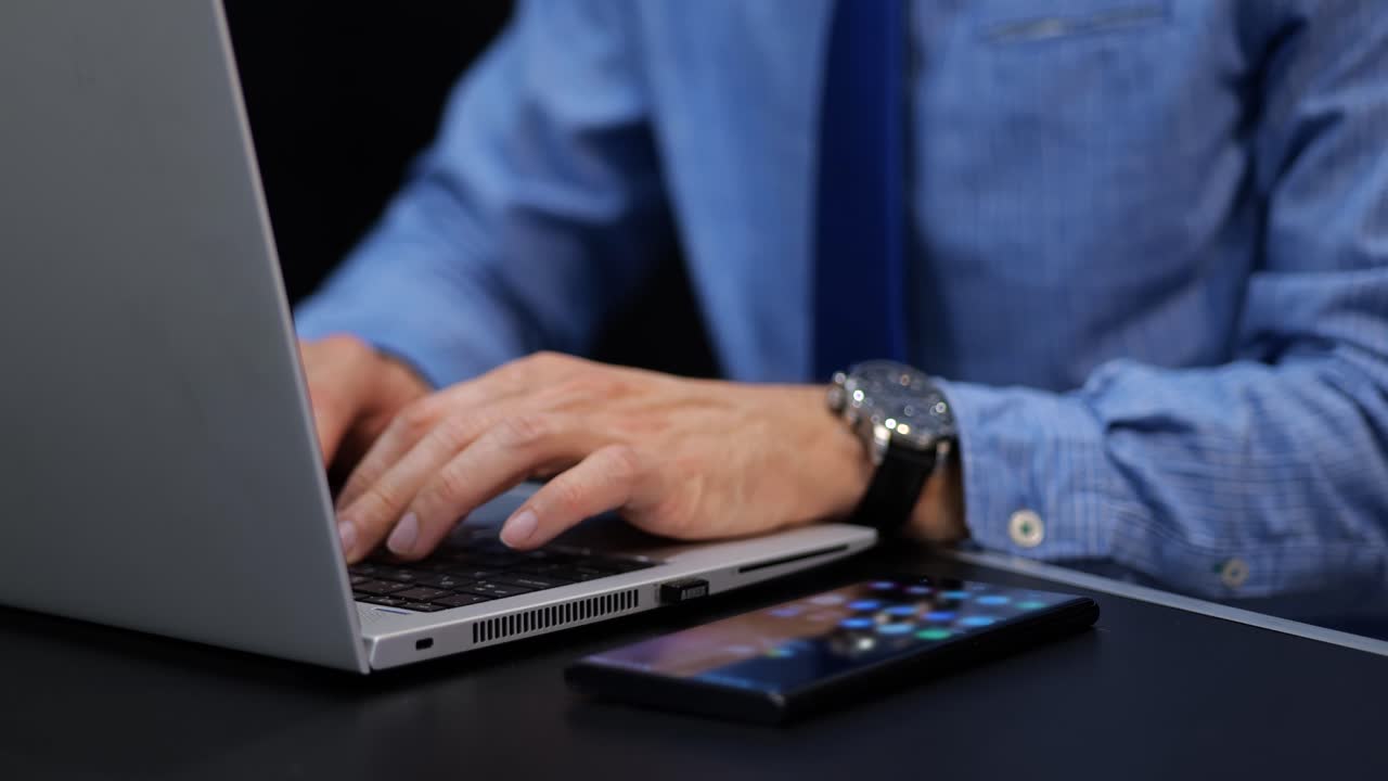Businessman working on laptop typing email with phone screen beside computer