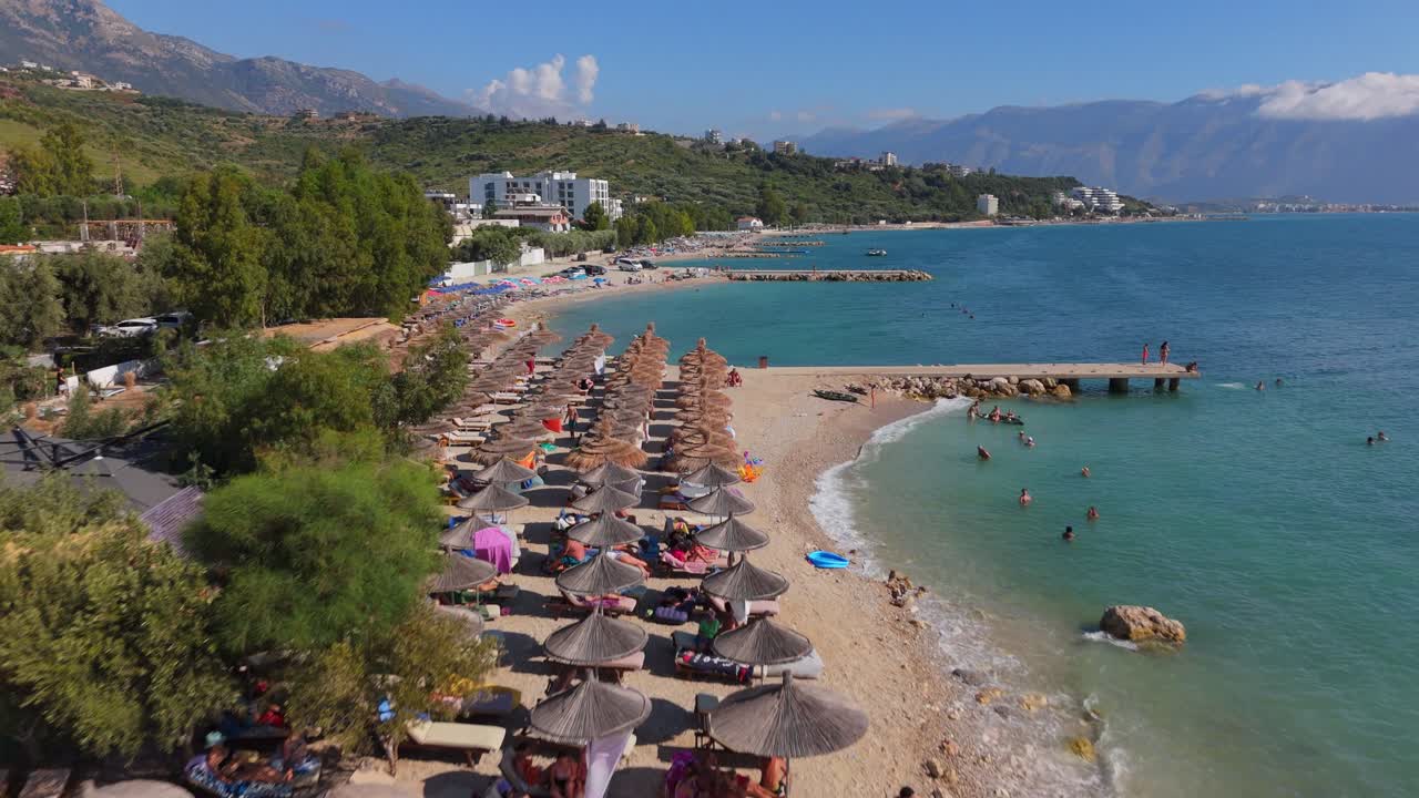 Crowded beach with umbrellas and people swimming in clear water on a sunny day