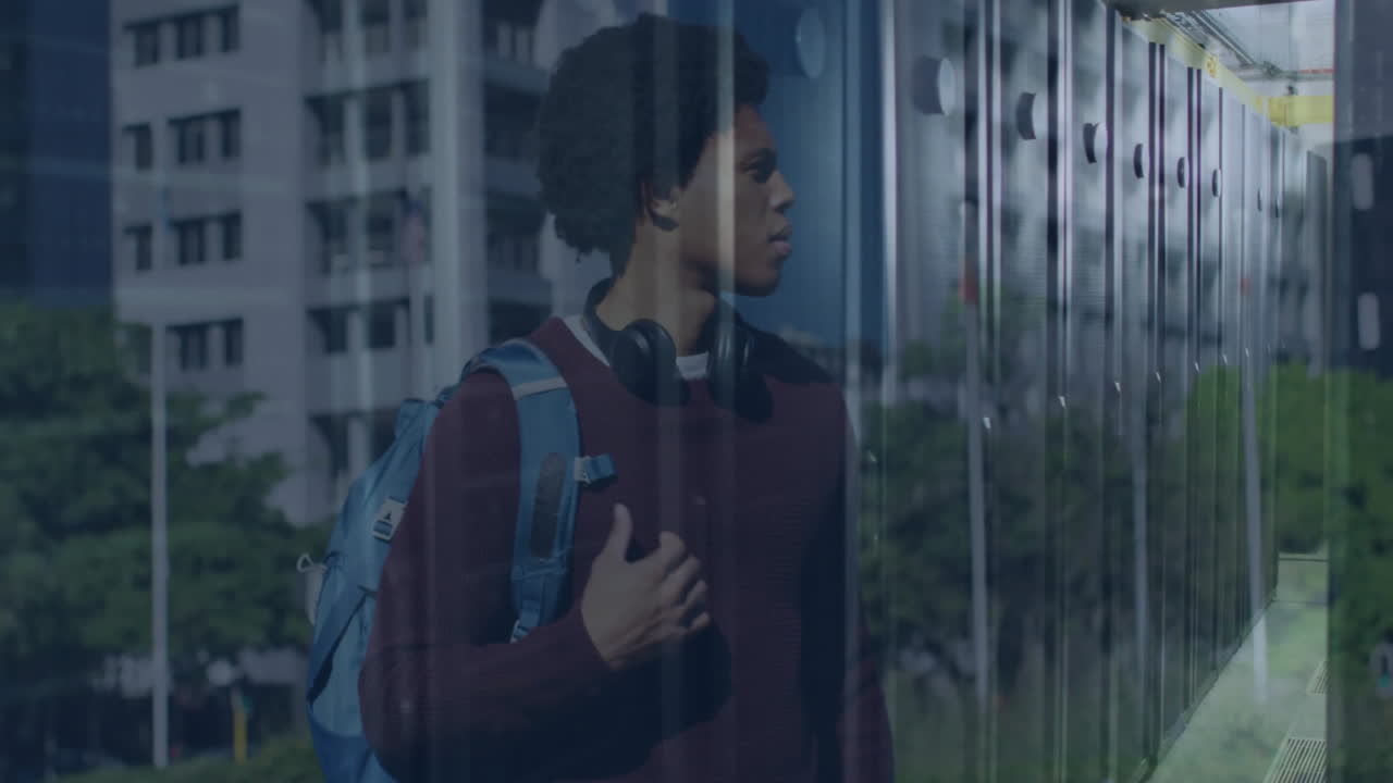 Standing near glass building, man with backpack and headphones looking thoughtful