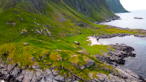 drone closing in on cabin at the foot of the mountain next to a beach