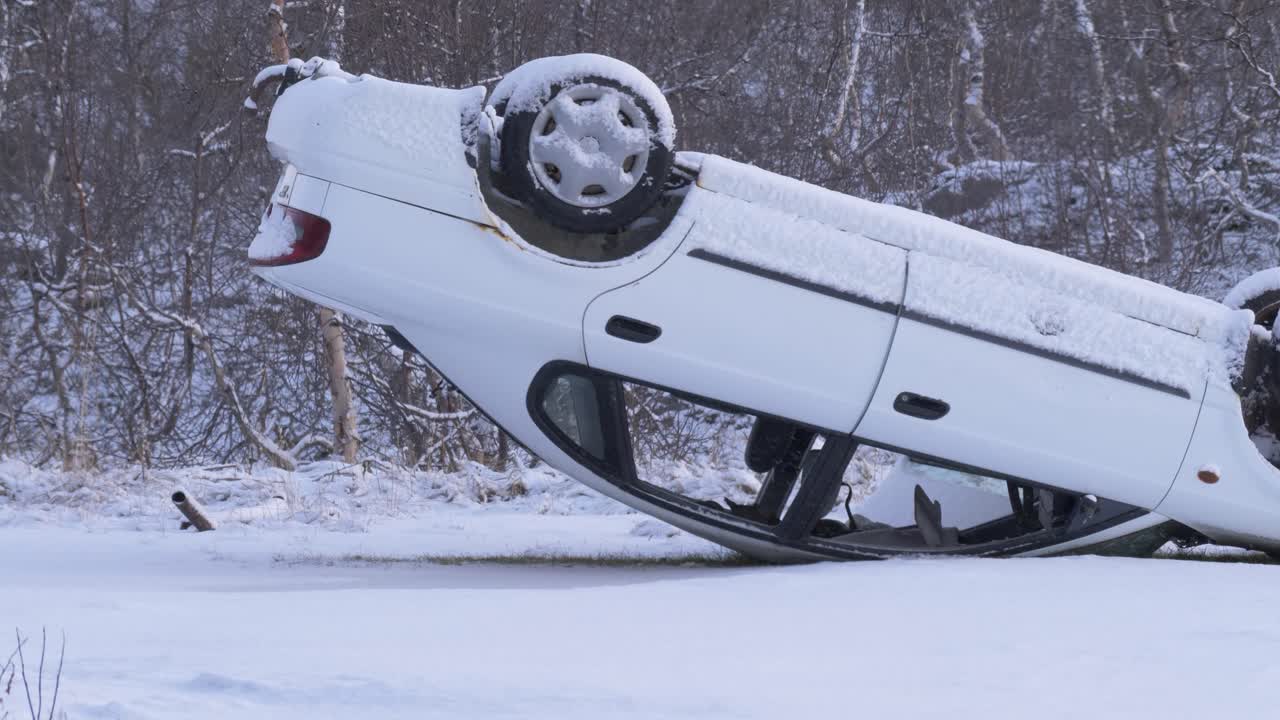 Car upside down in a serious accident on a frozen and snowy road amidst nordic forest - Static medium shot