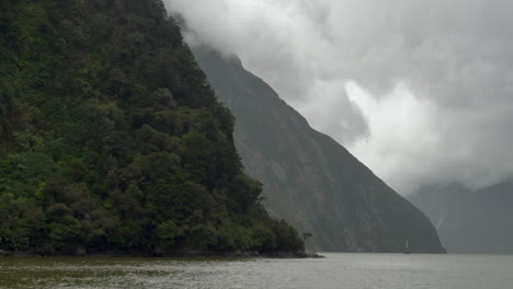 4K-footage-of-a-cloudy-Milford-Sound-with-a-boat-providing-scale-in-the-distance---Piopiotahi,-New-Zealand