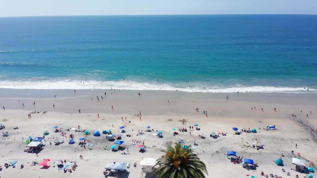 Tomada aérea panorâmica sobre uma praia de areia movimentada e lotada na Califórnia, EUA