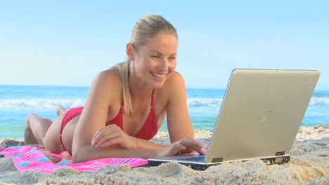 mujer rubia usando computadora portátil en la playa