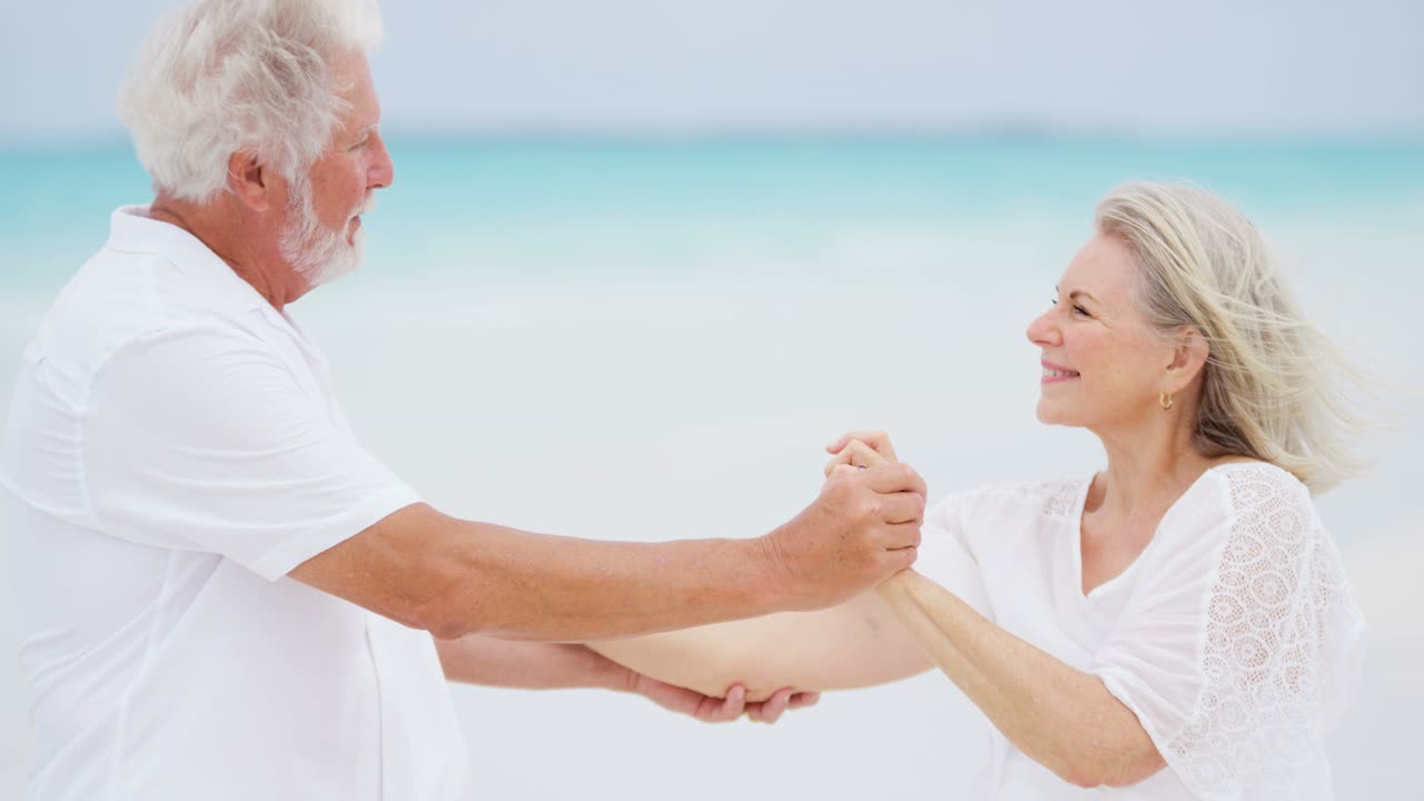 노인 백인 부부는 해변에서 춤을 추는  옷을 입고 있습니다.