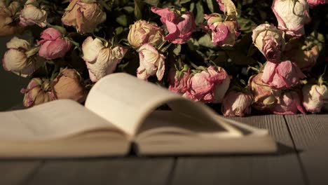 bouquet of withered rose flowers and open book on wooden table