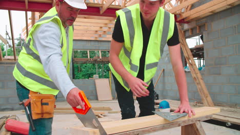 carpenter with male apprentice cutting wood on building site