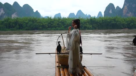 chinese hanfu girl fixing her hair while standing on bamboo raft by li river, xingping