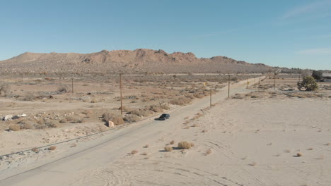 Slow-motion-drone-shot-of-a-car-going-through-a-desert-in-Palmdale,-California-on-a-bright-clear-day