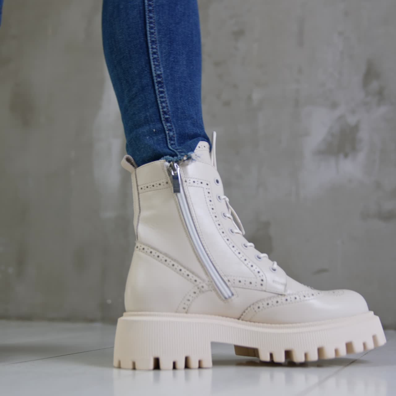 New milk-white army boots on massive soles and with laces. Model in jeans walks close to the camera demonstrating footwear from different sides. Low angle view