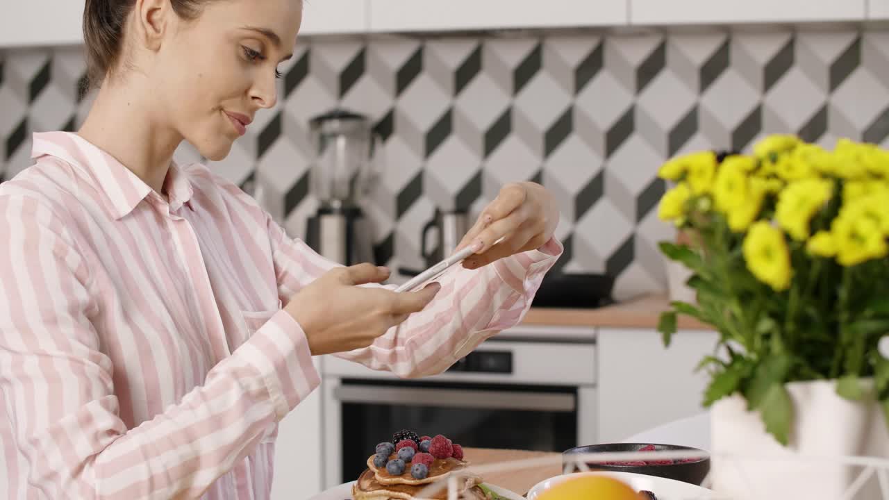 mujer fotografiando panqueques con frutas durante el desayuno en la cocina