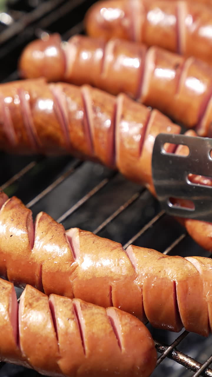 Hot tasty sausages on grill. Cook turning over almost ready sausages for the picnic. Frying food on charcoals in the garden. Close-up. Vertical video